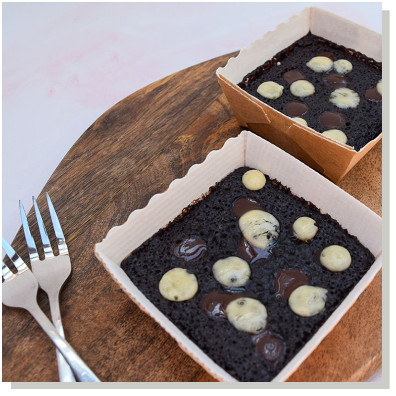 two trays of vegan chocolate brownies on a wooden surface with two forks alongside