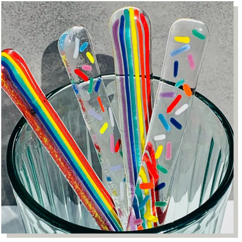 hand painted glass drink stirrers in a glass, the colours of the drink stirrers are rainbow colours